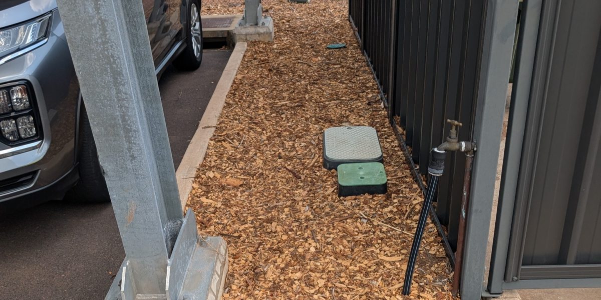Wood chip mulch installation around poles and garden bed at a Palmerston property.